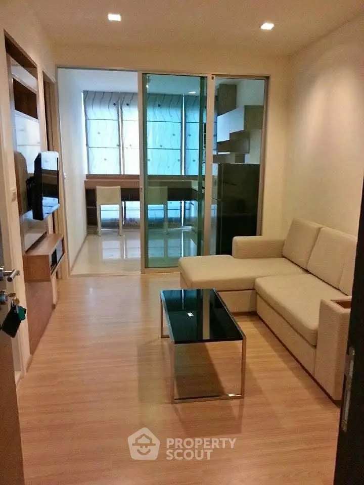Modern living room with glass coffee table and beige sofa, featuring a sleek wooden floor and glass partition.