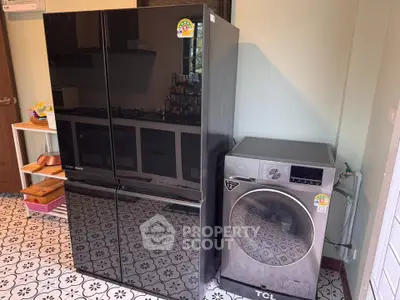 Modern kitchen with sleek black fridge and advanced washing machine on patterned floor.
