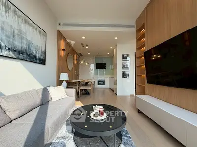 Modern living room with stylish decor and open kitchen layout, featuring a large TV and elegant lighting.
