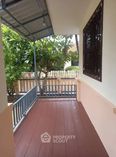 Charming garden view from a cozy balcony with wooden flooring and metal railing.