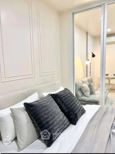 Modern bedroom with plush pillows and elegant decor, featuring a glass partition to a cozy living area.