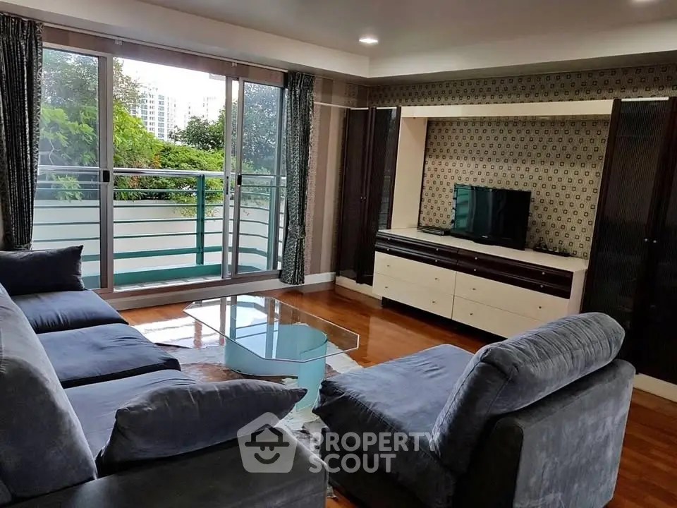 Spacious living room with modern furniture and large windows offering a lush green view.