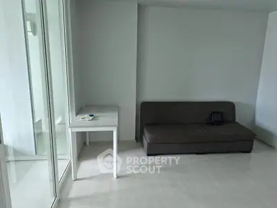 Minimalist living room with sofa and table, featuring large glass doors for natural light.