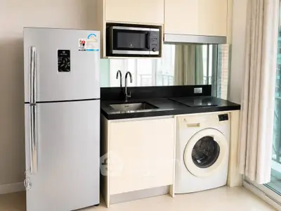 Modern compact kitchen with fridge, microwave, and washing machine in sleek apartment.