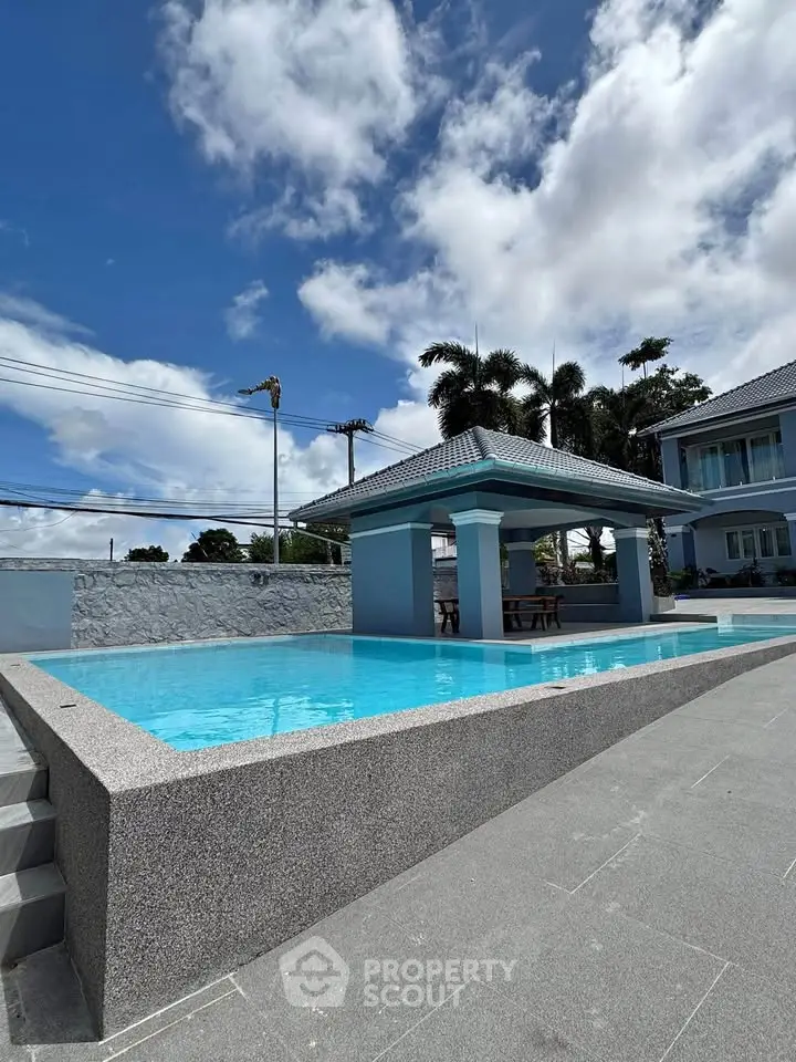 Luxurious poolside view of modern villa with clear blue skies and lush greenery.
