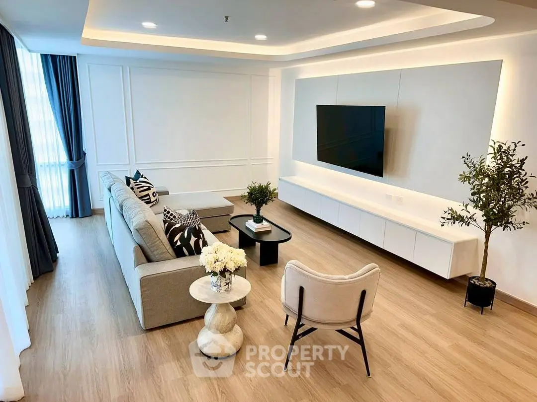 Modern living room with stylish decor and large wall-mounted TV, featuring elegant furniture and natural light.