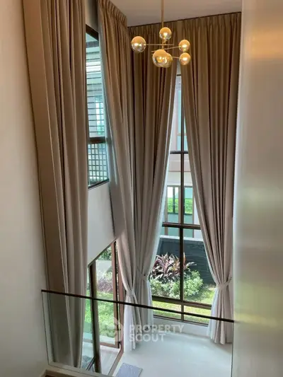 Elegant double-height living room with floor-to-ceiling windows and modern chandelier.