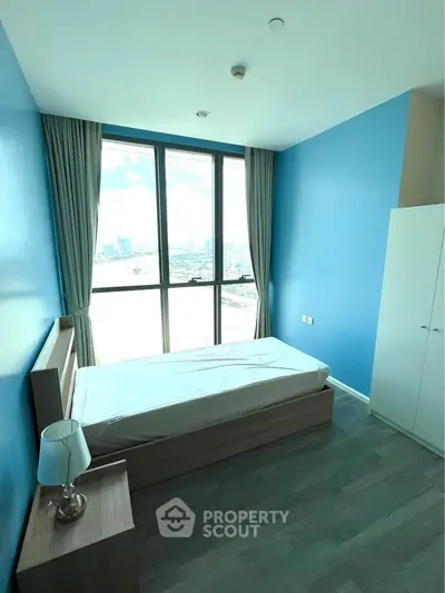 Bright bedroom with large window offering stunning city views, featuring modern furnishings and blue accent wall.