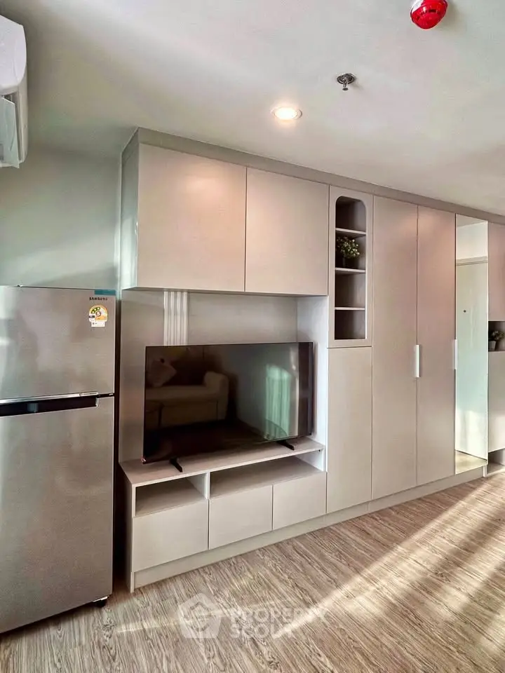 Modern living room with sleek built-in cabinets and flat-screen TV, featuring a compact refrigerator.