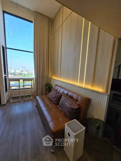 Modern living room with leather sofa and city view, featuring stylish lighting and floor-to-ceiling windows.