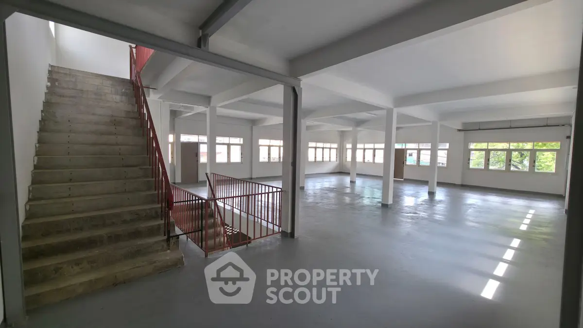Spacious open-plan interior with large windows and staircase, ideal for versatile use.