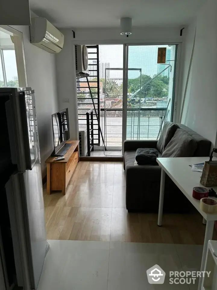 Modern living room with balcony and city view, featuring sleek furniture and natural light.