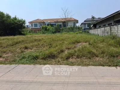 Spacious residential plot with lush greenery and modern houses in the background.