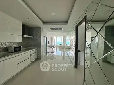 Luxurious modern kitchen with sleek design and ocean view, featuring high-end appliances and glossy finishes.