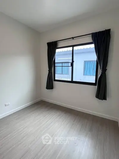 Bright empty room with large window and modern flooring, perfect for customization.