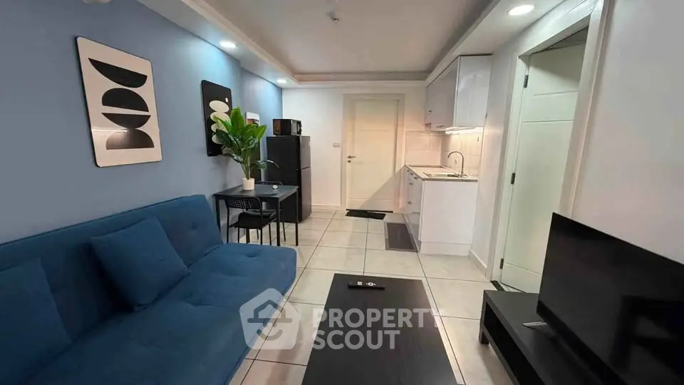 Modern living room with sleek furniture and compact kitchen in open layout apartment.
