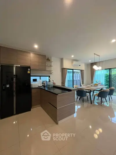 Modern kitchen with sleek cabinetry and dining area, featuring large windows and stylish lighting.