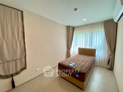 Spacious bedroom with large window and elegant curtains in modern apartment.