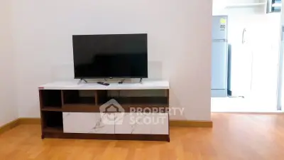 Modern living room with sleek TV stand and flat-screen TV, adjacent to a bright kitchen area.