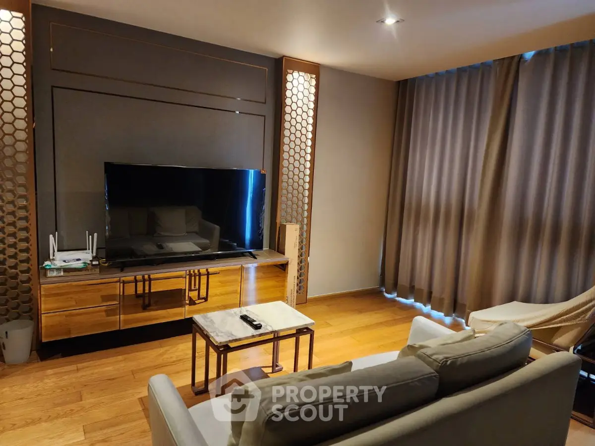 Modern living room with sleek TV setup and stylish furniture, featuring wooden flooring and elegant curtains.