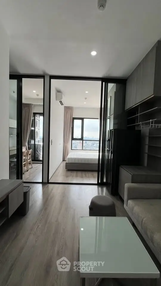 Modern apartment interior with open living room and bedroom, featuring large windows and sleek furniture.