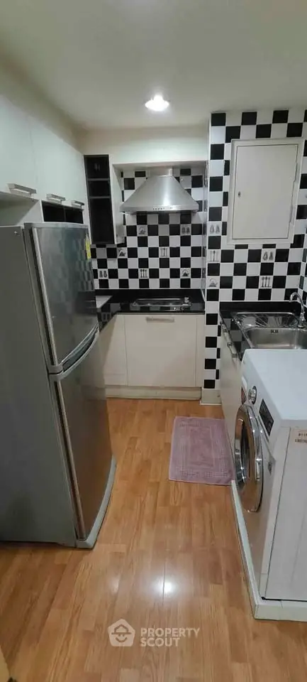 Modern kitchen with checkered backsplash, stainless steel appliances, and wooden flooring.