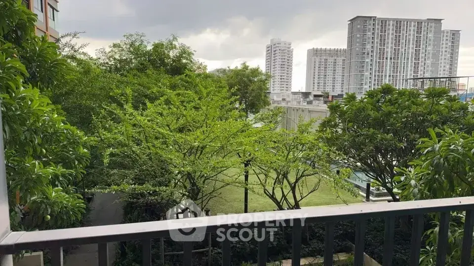 Scenic balcony view with lush greenery and modern high-rise buildings.