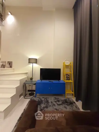 Modern living room with stylish decor, featuring a blue TV stand, yellow ladder shelf, and cozy lighting.