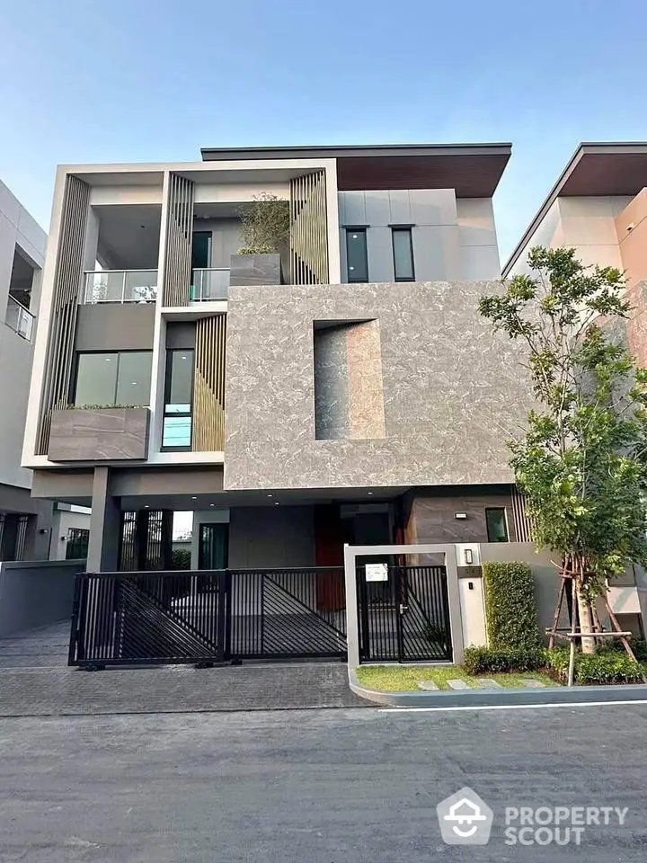 Modern three-story house with sleek facade and gated entrance in upscale neighborhood.