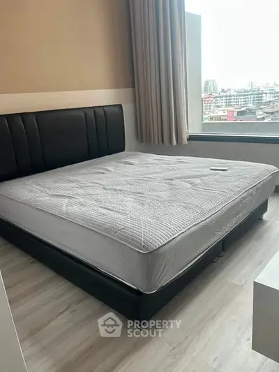 Modern bedroom with large window offering city view, featuring sleek black bed and minimalist decor.