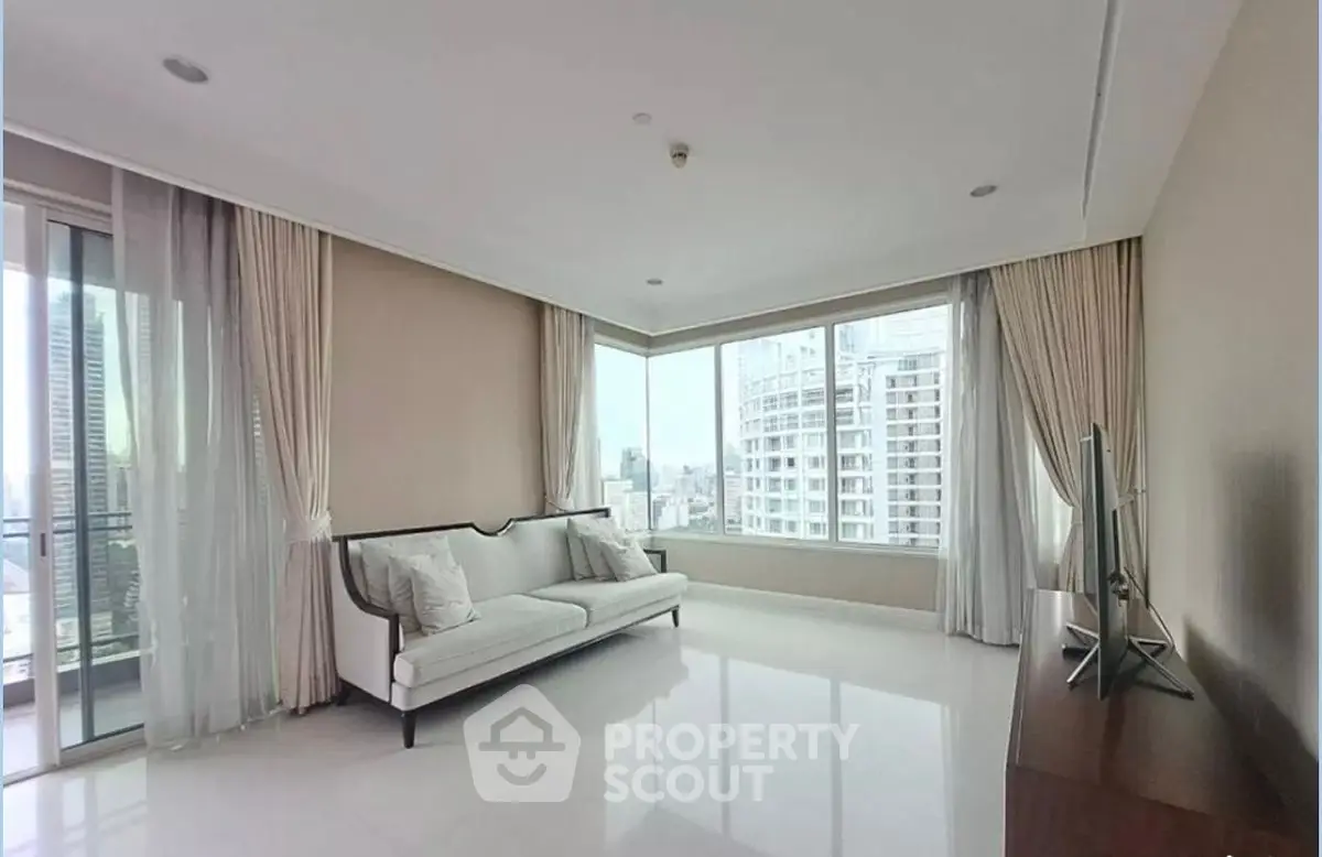 Spacious living room with large windows and city view, featuring elegant sofa and modern TV setup.