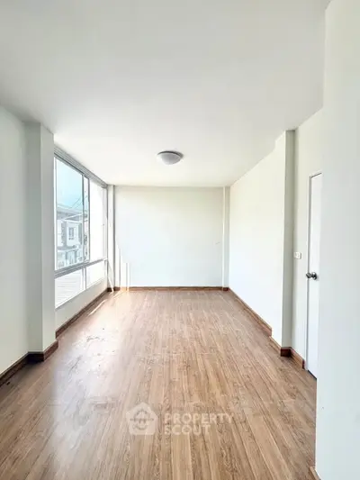 Spacious empty room with large windows and wooden flooring, perfect for customization.