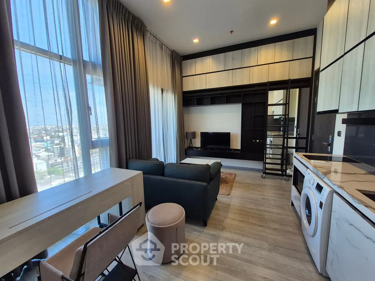 Modern living room with open kitchen, featuring sleek furniture and large windows for natural light.
