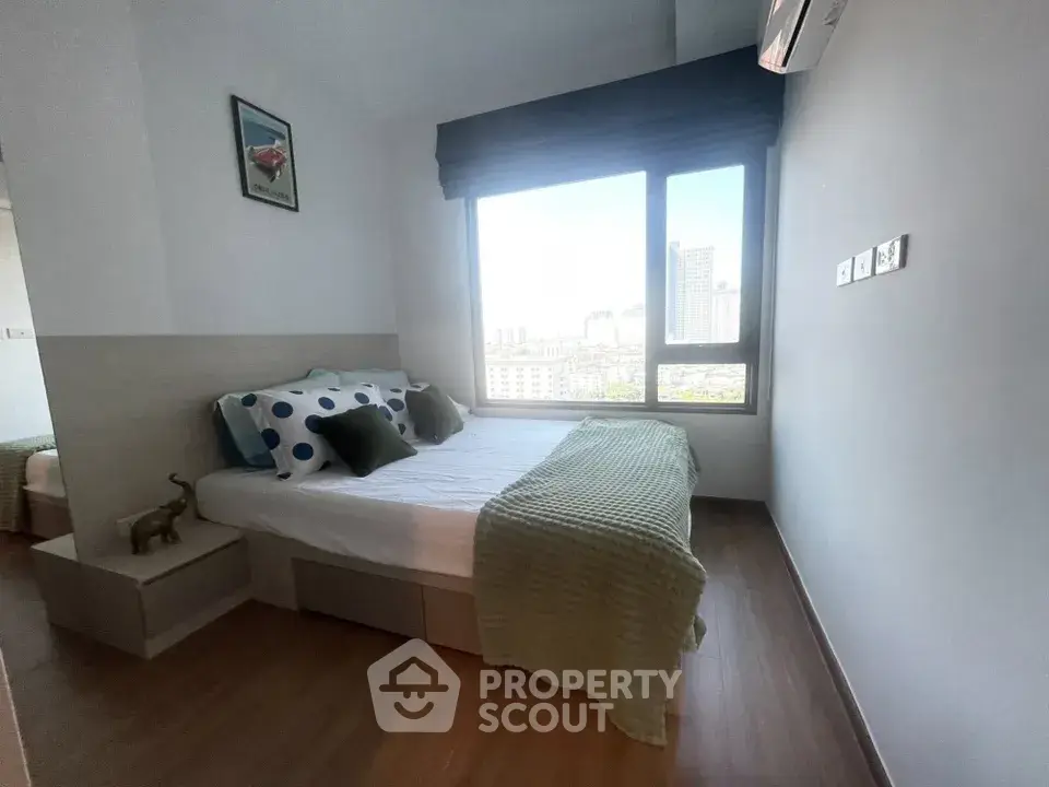 Cozy bedroom with large window offering city view, modern decor, and wooden flooring.