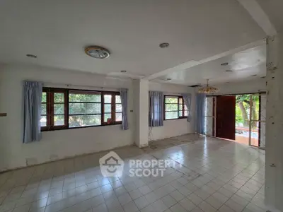 Spacious living room with large windows and tiled flooring, offering abundant natural light and garden views.
