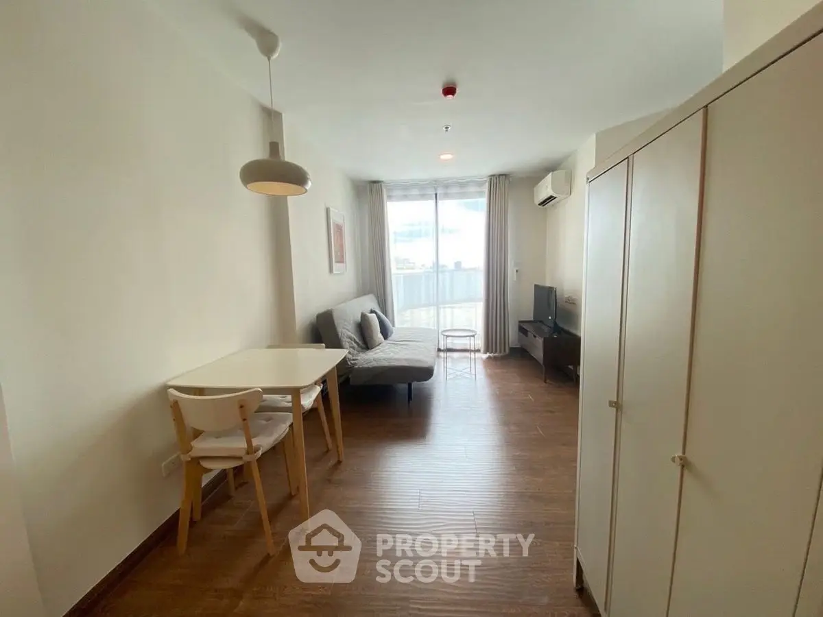 Cozy living room with modern furniture and natural light, featuring a small dining area and balcony access.