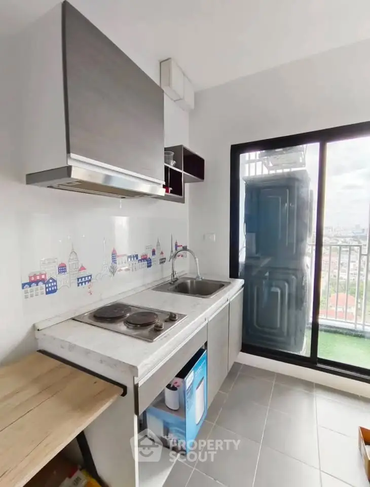 Modern kitchen with electric stove and balcony view in urban apartment.