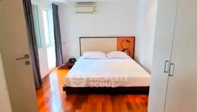 Spacious bedroom with wooden flooring and large windows in modern apartment.