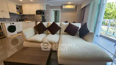 Spacious living room with modern kitchen and balcony access, featuring a cozy sectional sofa.