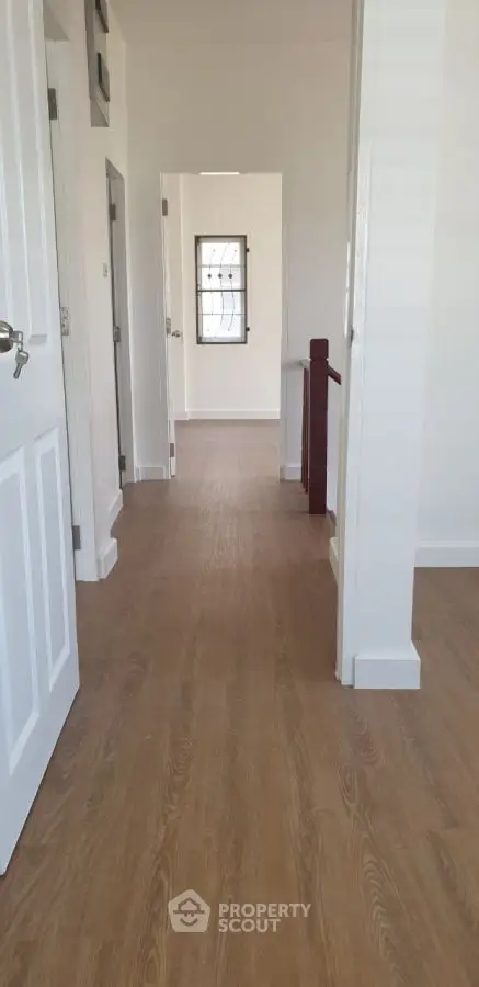 Bright hallway with wooden flooring and white walls, leading to multiple rooms.