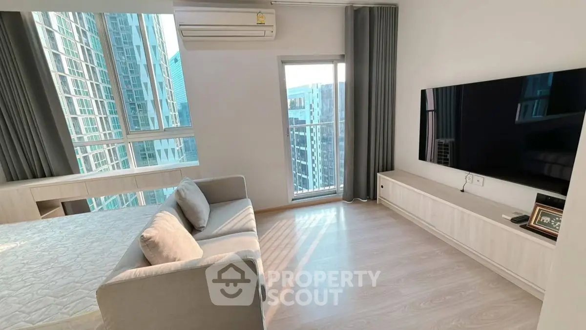 Modern living room with large TV, cozy sofa, and city view from window.