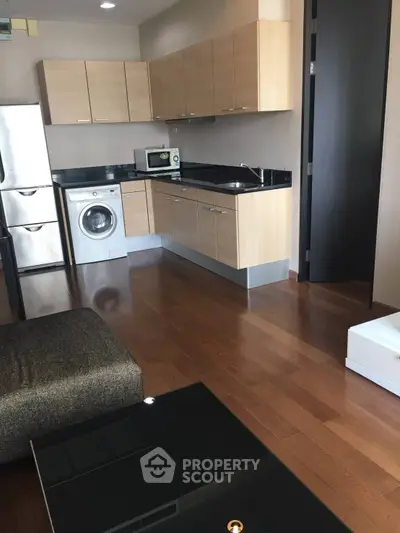 Modern kitchen with wooden cabinets, washing machine, and sleek appliances in open layout.