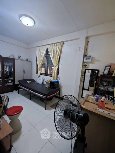 Cozy bedroom with natural light, fan, and simple furnishings, ideal for comfortable living.