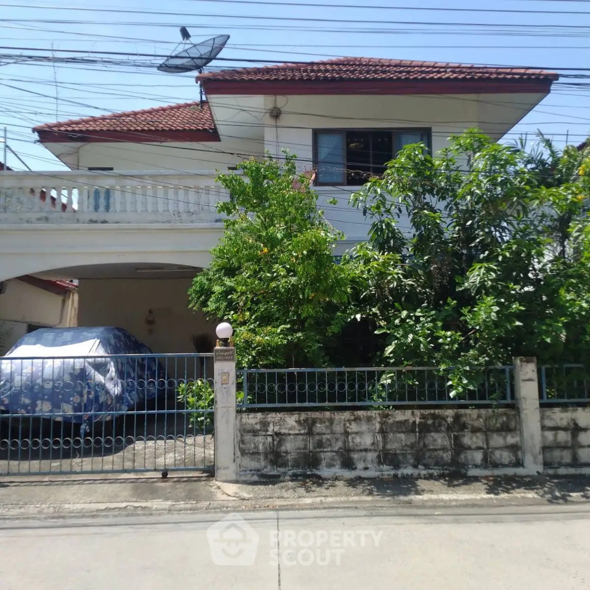 Charming two-story house with red roof, lush greenery, and gated driveway in a serene neighborhood.
