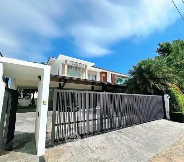 Stunning modern house with sleek gate and lush greenery under a clear blue sky.