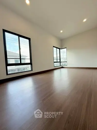 Spacious empty room with large windows and wooden flooring, perfect for customization.