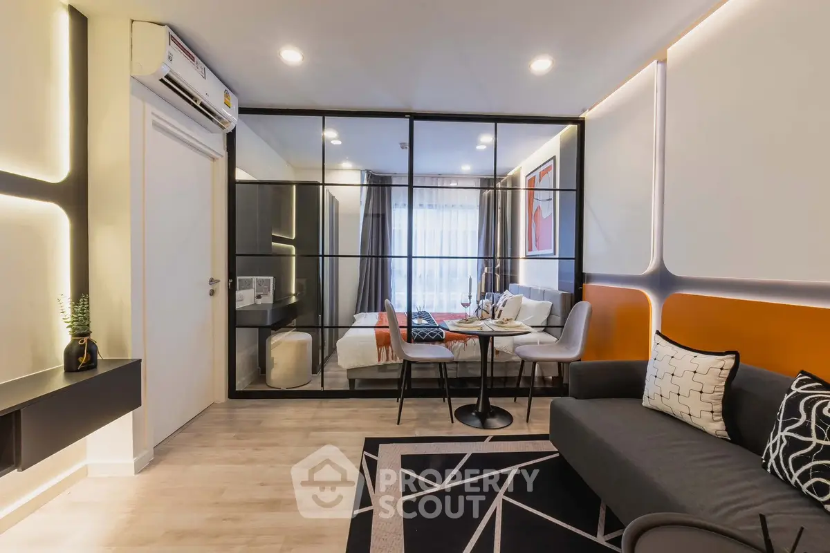 Modern living room with stylish decor and glass partition leading to a cozy bedroom.