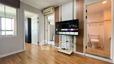 Modern living room with wooden flooring, wall-mounted TV, and adjacent bathroom in a stylish apartment.