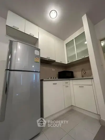 Modern compact kitchen with sleek white cabinets and stainless steel fridge.