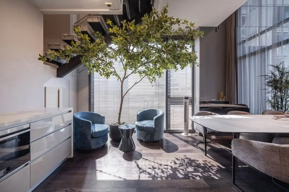 Modern living room with stylish furniture and indoor tree, featuring natural light and elegant decor.